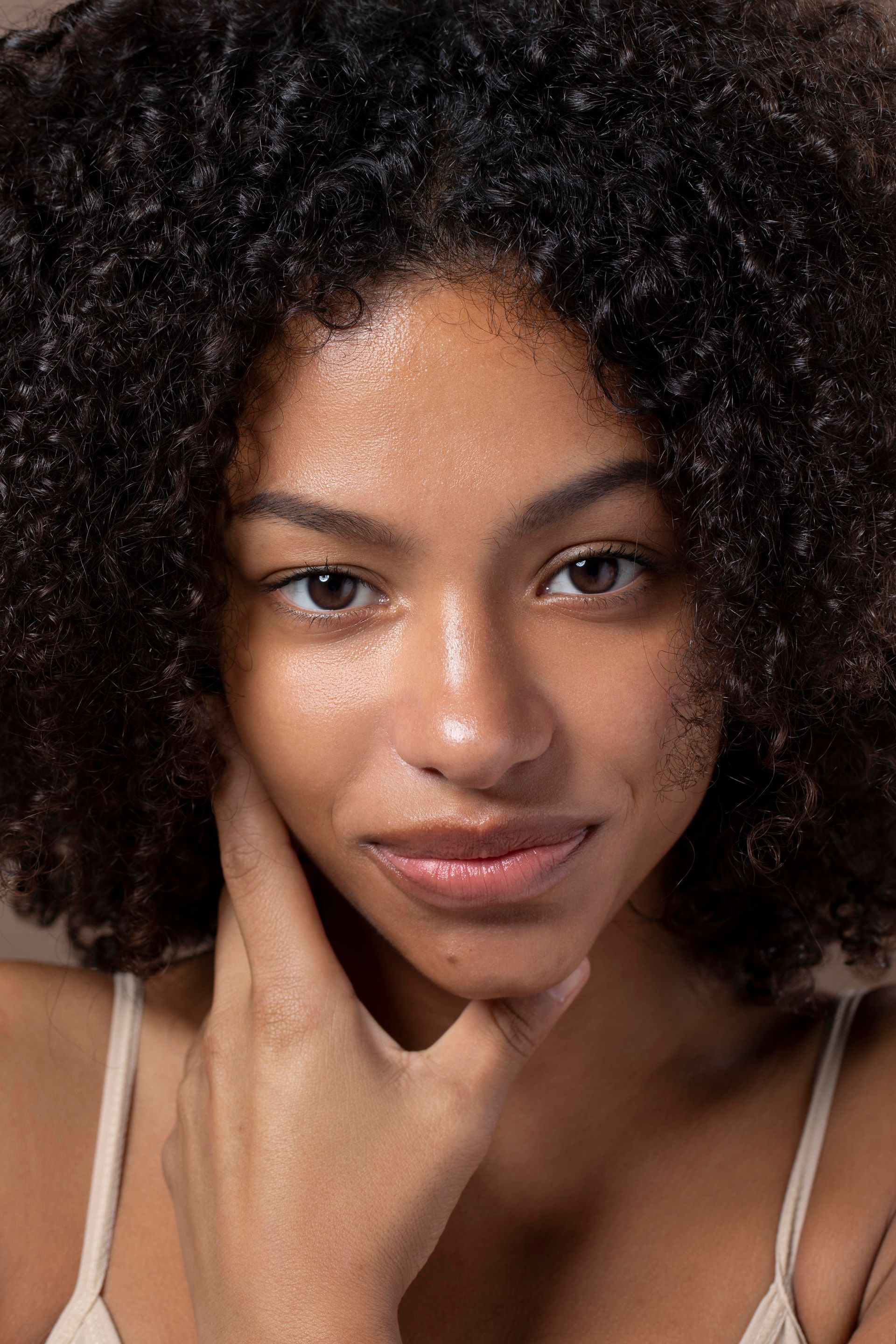 A woman with curly hair is touching her face with her hand.