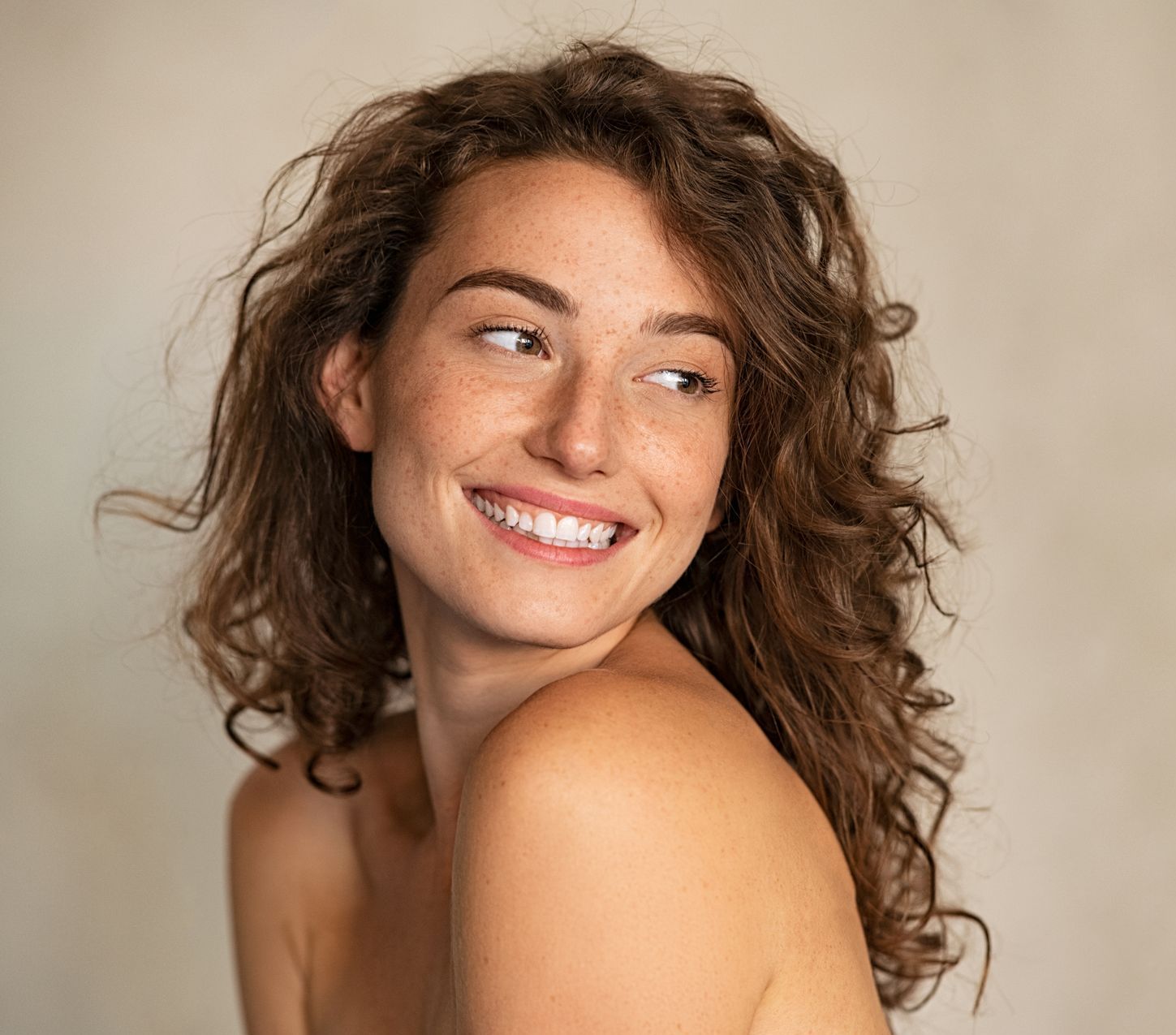 A woman with curly hair is smiling and looking over her shoulder.