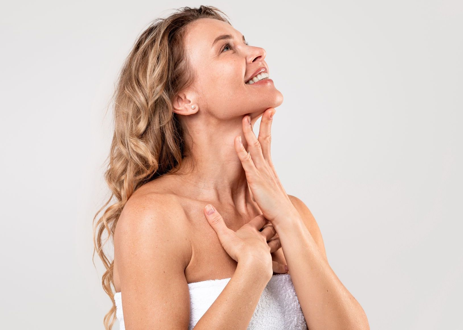 Woman in white towel touching her neck, smiling, looking up.