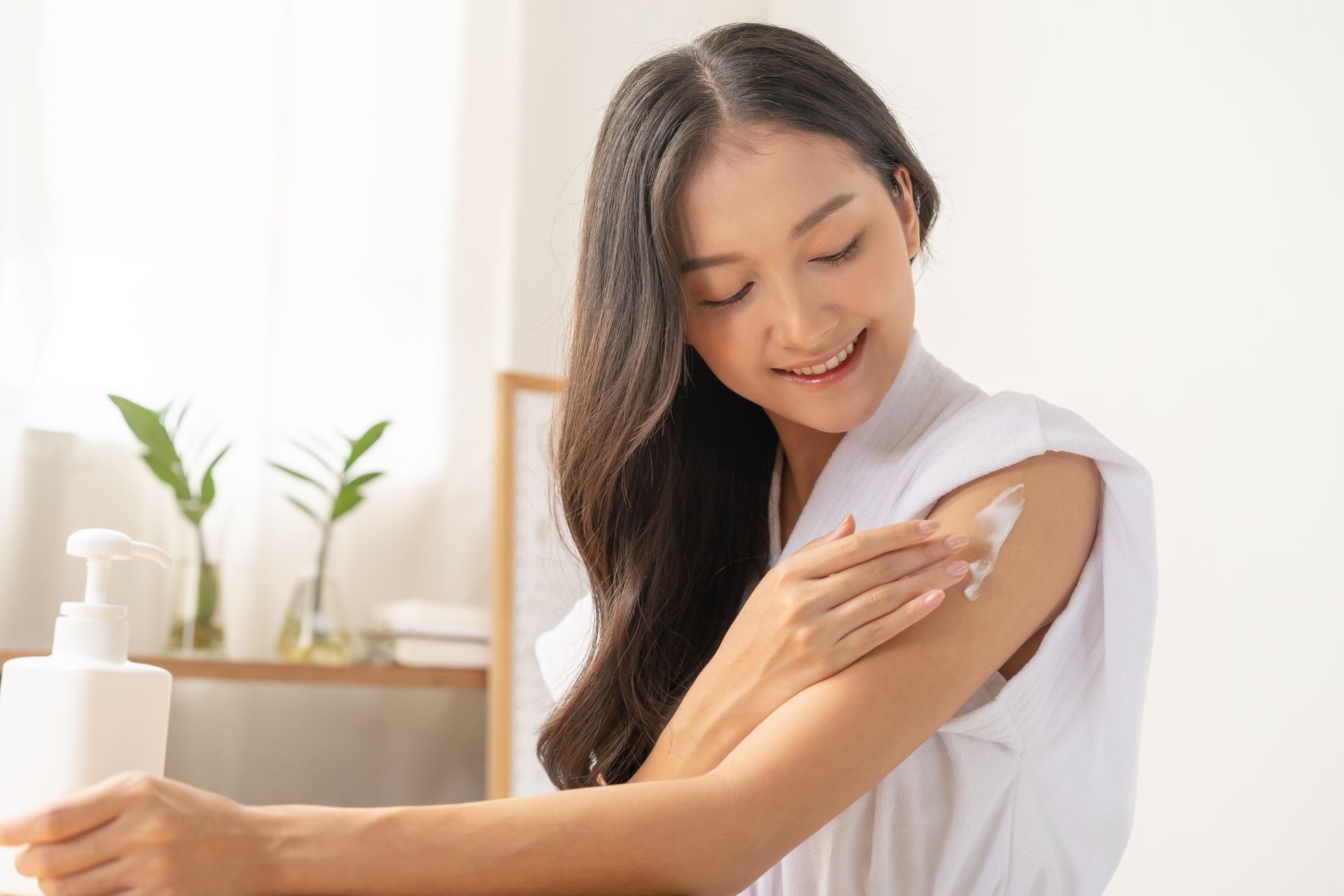 A woman is applying lotion to her arm in a bathroom.