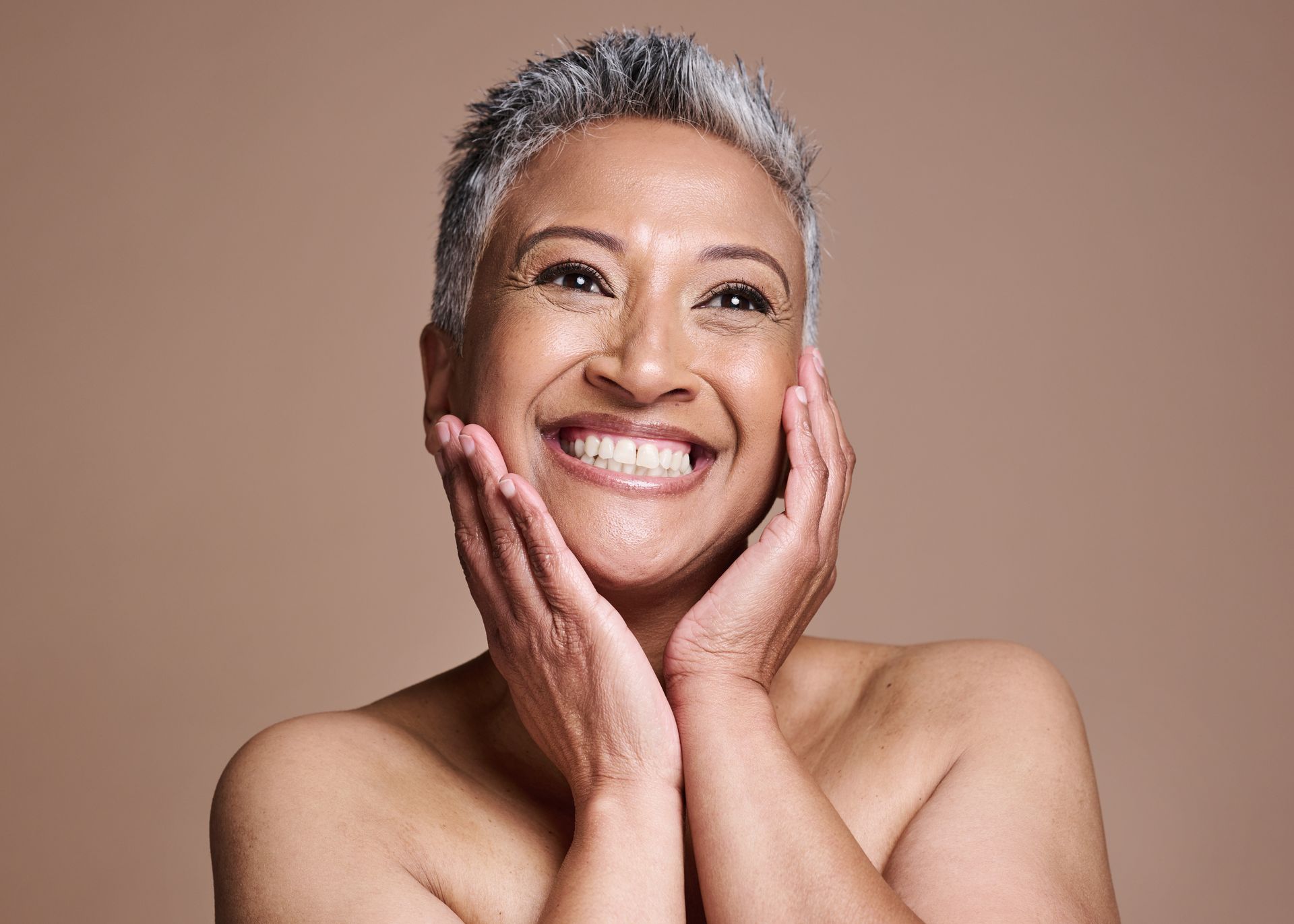 A shirtless woman is smiling with her hands on her face.