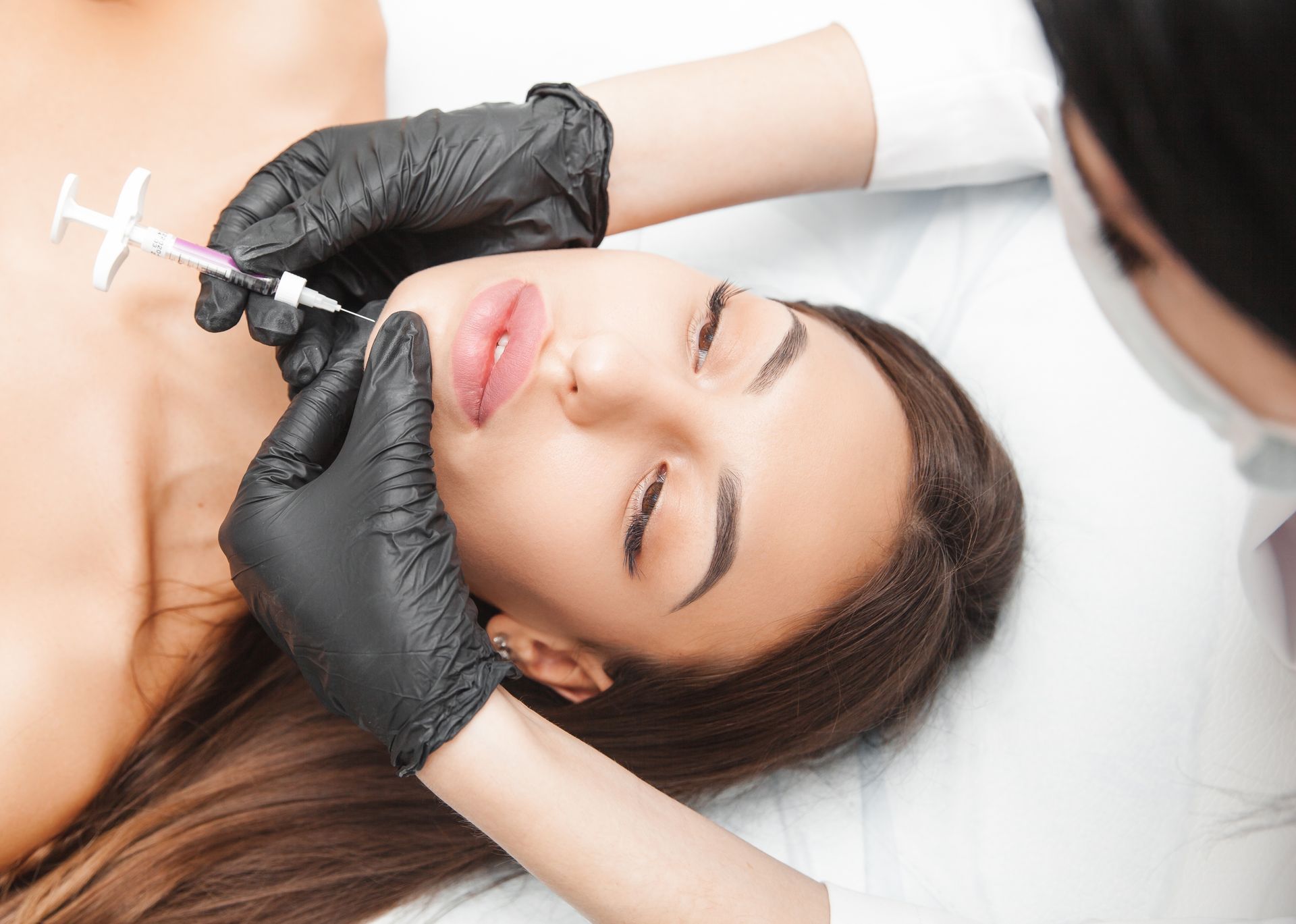 Woman receiving lip filler injections; close-up of the procedure in a medical setting.