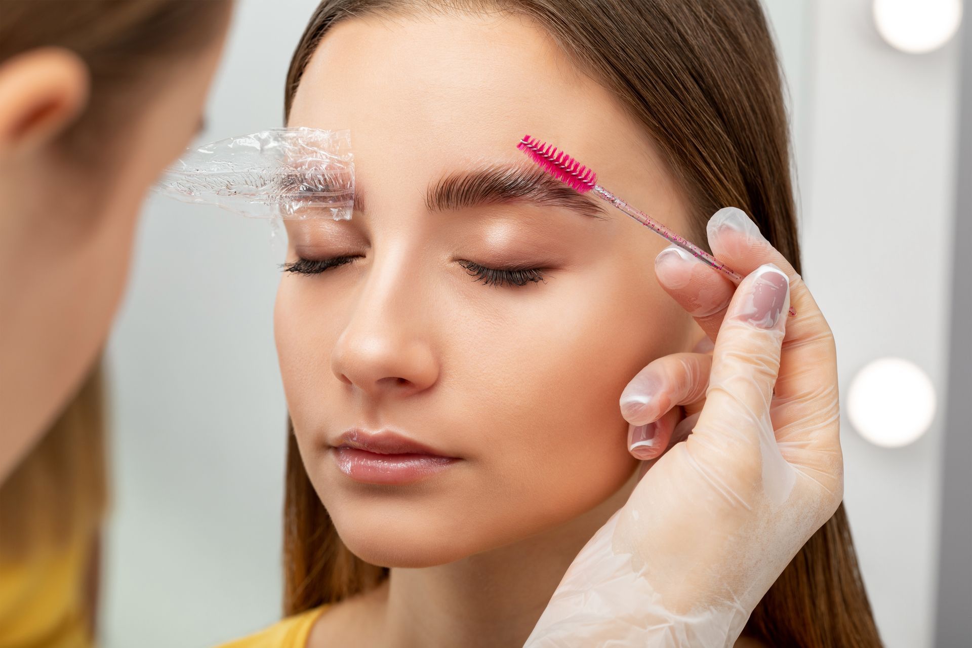 A woman is getting her eyebrows painted by a makeup artist.