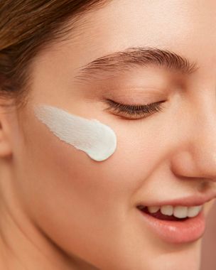 A close up of a woman applying cream to her face.