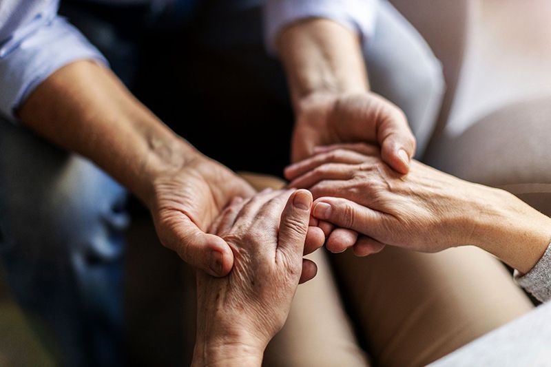 Hands clasped together in a supportive group gesture on a sofa