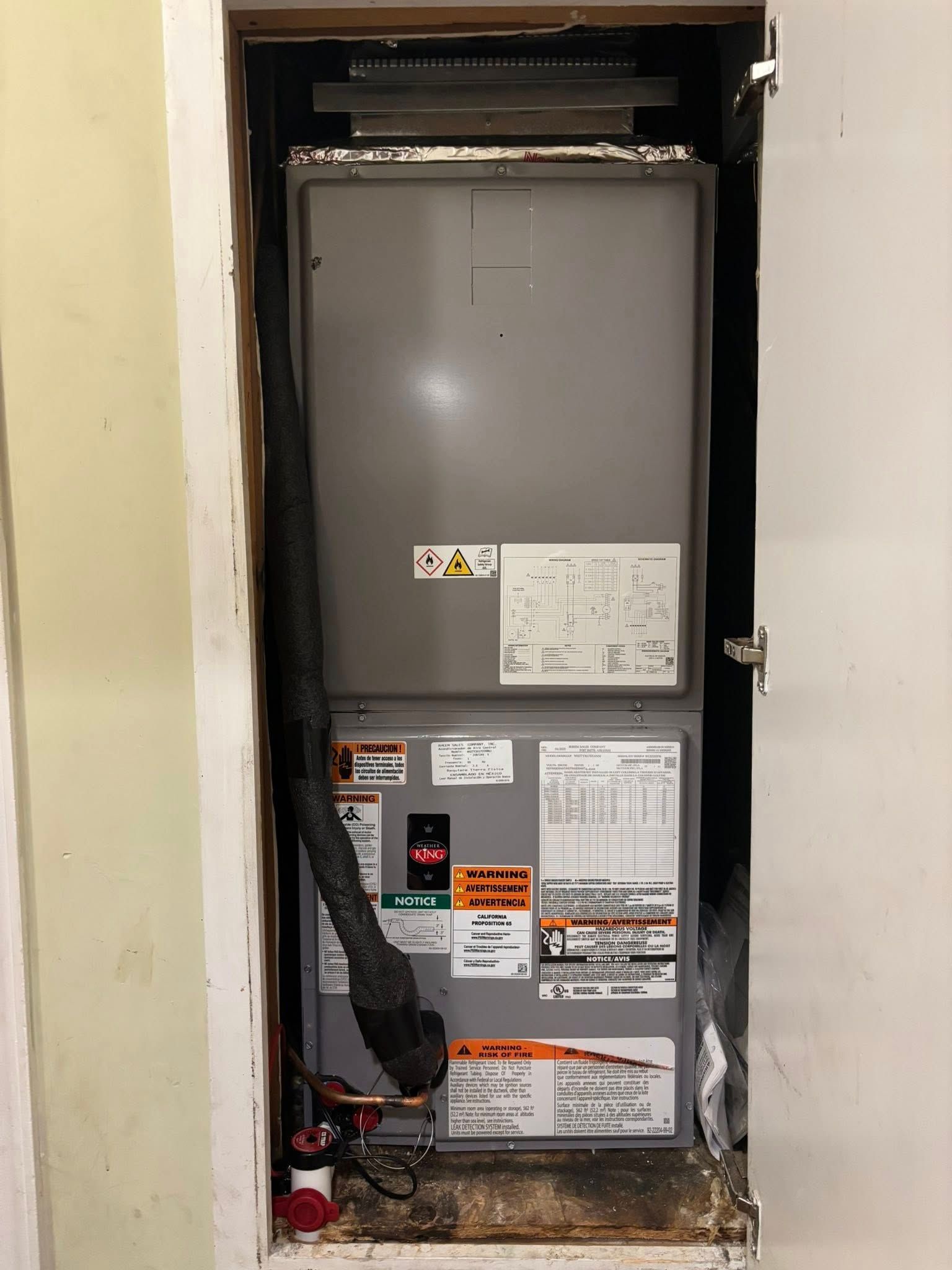Gray HVAC unit inside a closet with exposed black ducting and utility labels on the front.