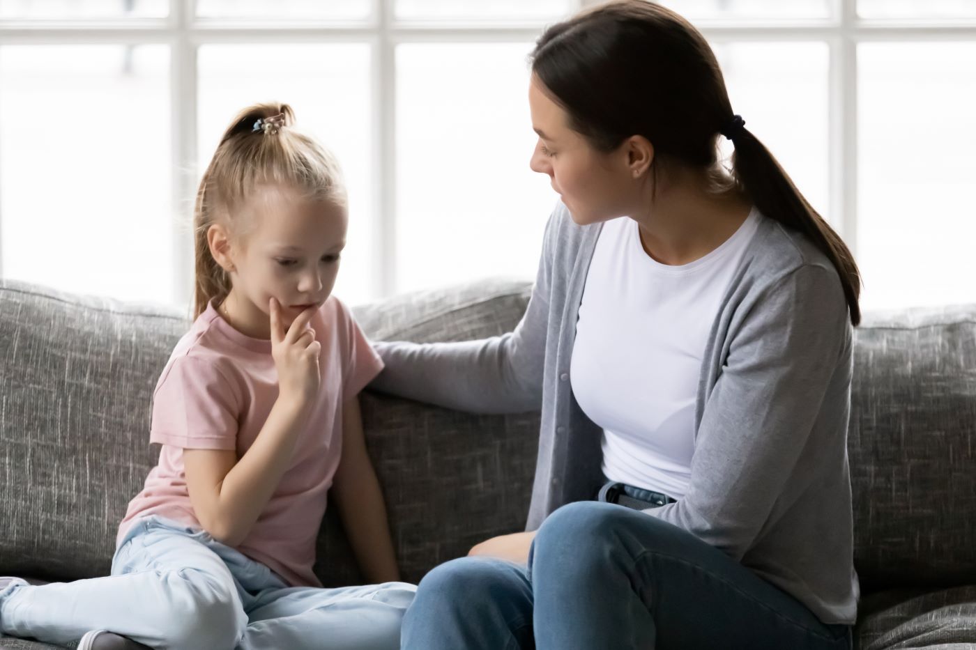 A woman is sitting on a couch talking to a little girl.