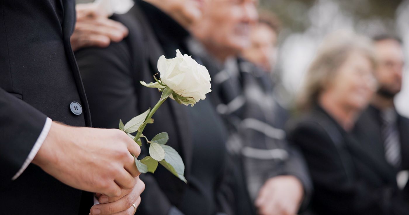 A man is holding a white rose at a funeral.