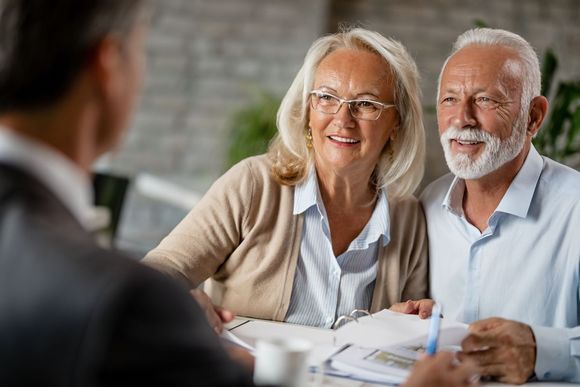 An elderly couple is sitting at a table talking to a man.