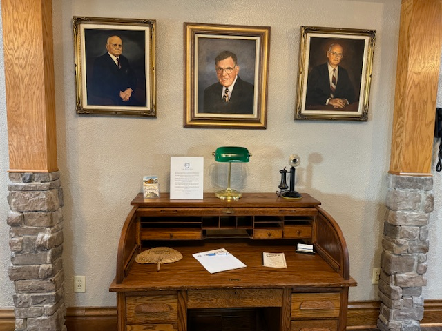 Three portraits of men are hanging on a wall above a desk