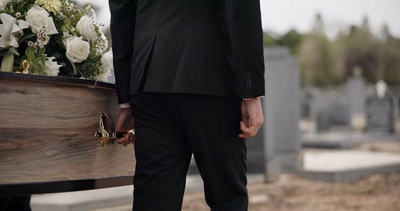 A man in a suit is carrying a coffin in a cemetery.