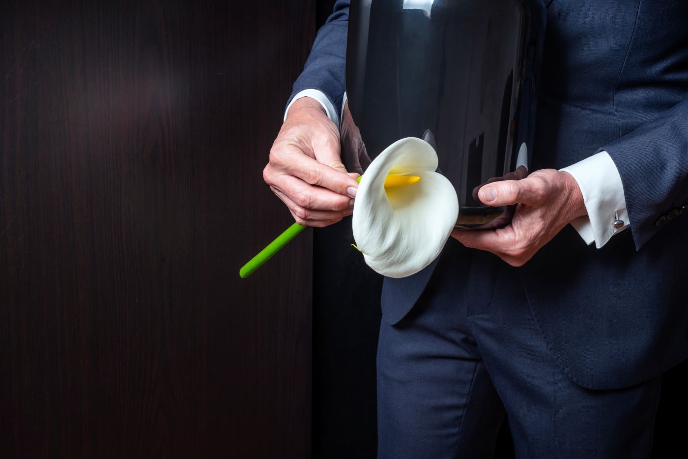 A man in a suit is holding a vase and a flower.