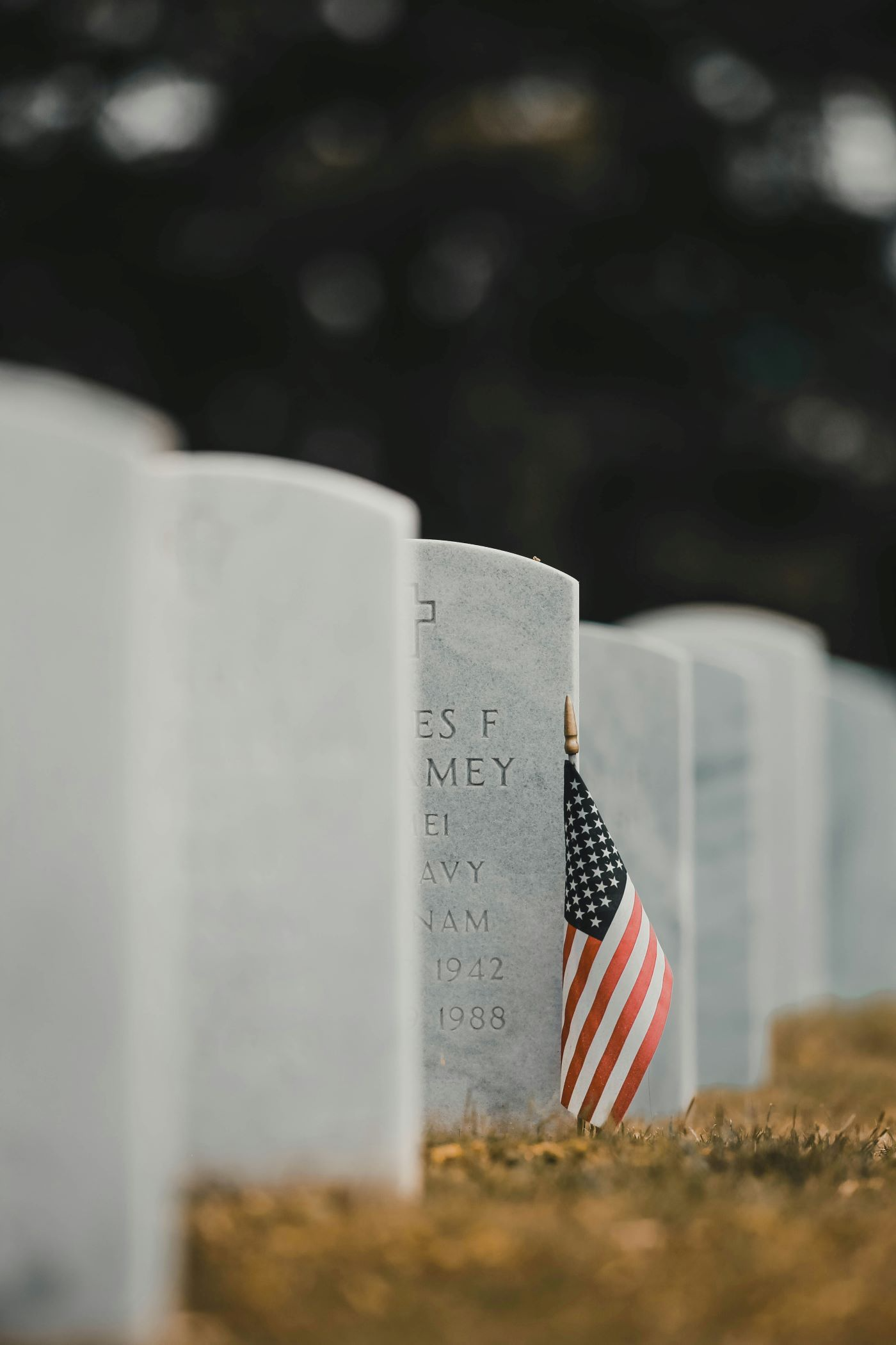 A small american flag is sitting on a grave in a cemetery.