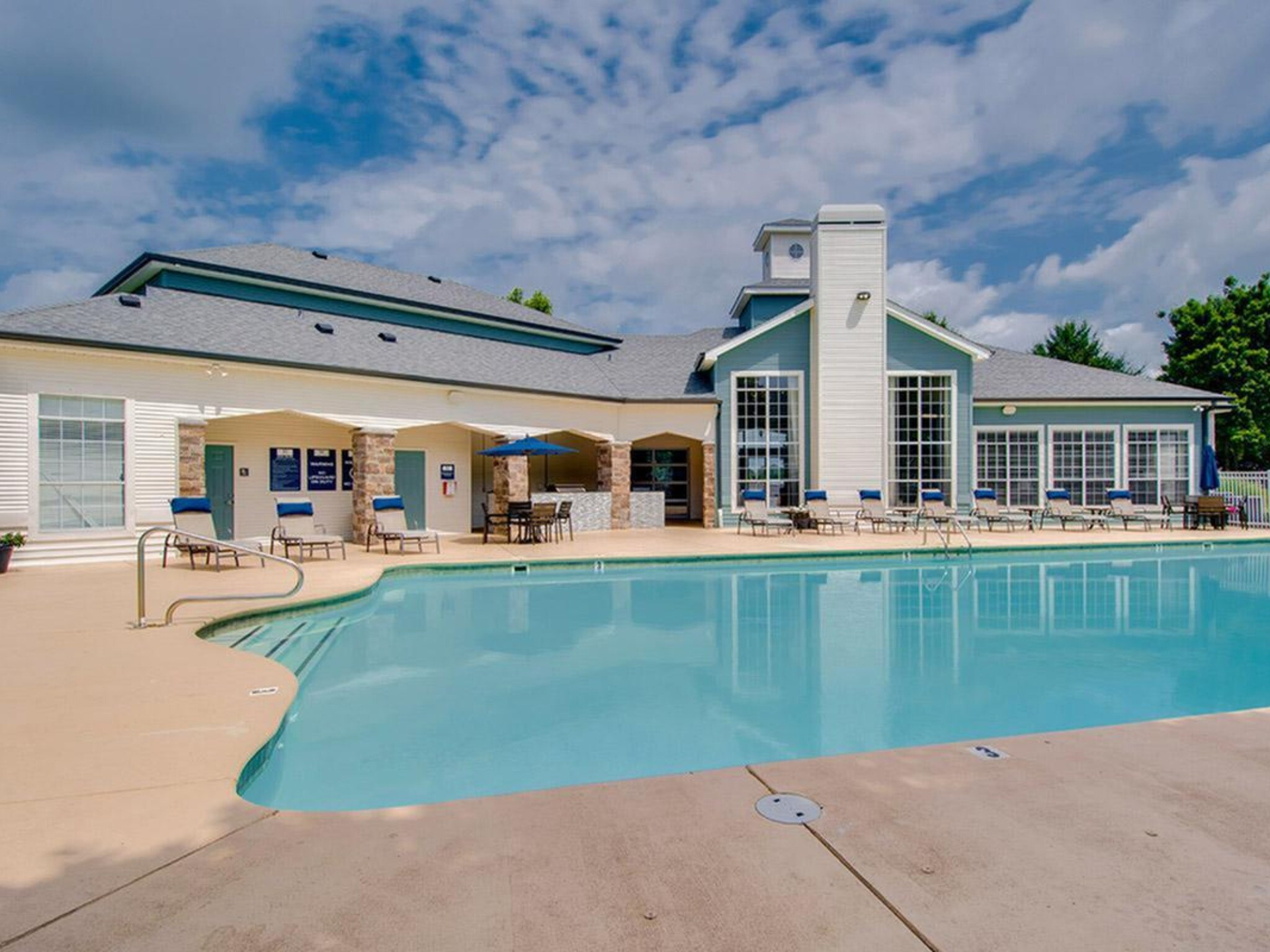 A swimming pool with a light blue surface in front of a light blue building with a gray roof, on a sunny day at Scout Landing.