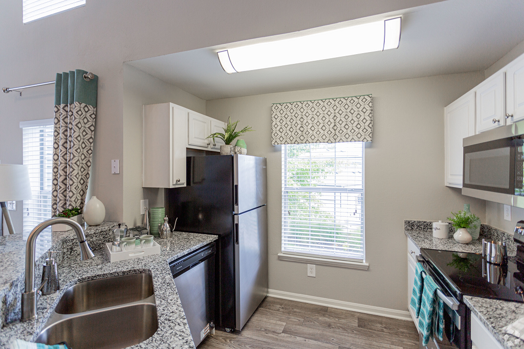 A modern kitchen with granite countertops, white cabinets, and stainless steel appliances. A window is centered above the sink at Scout Landing.