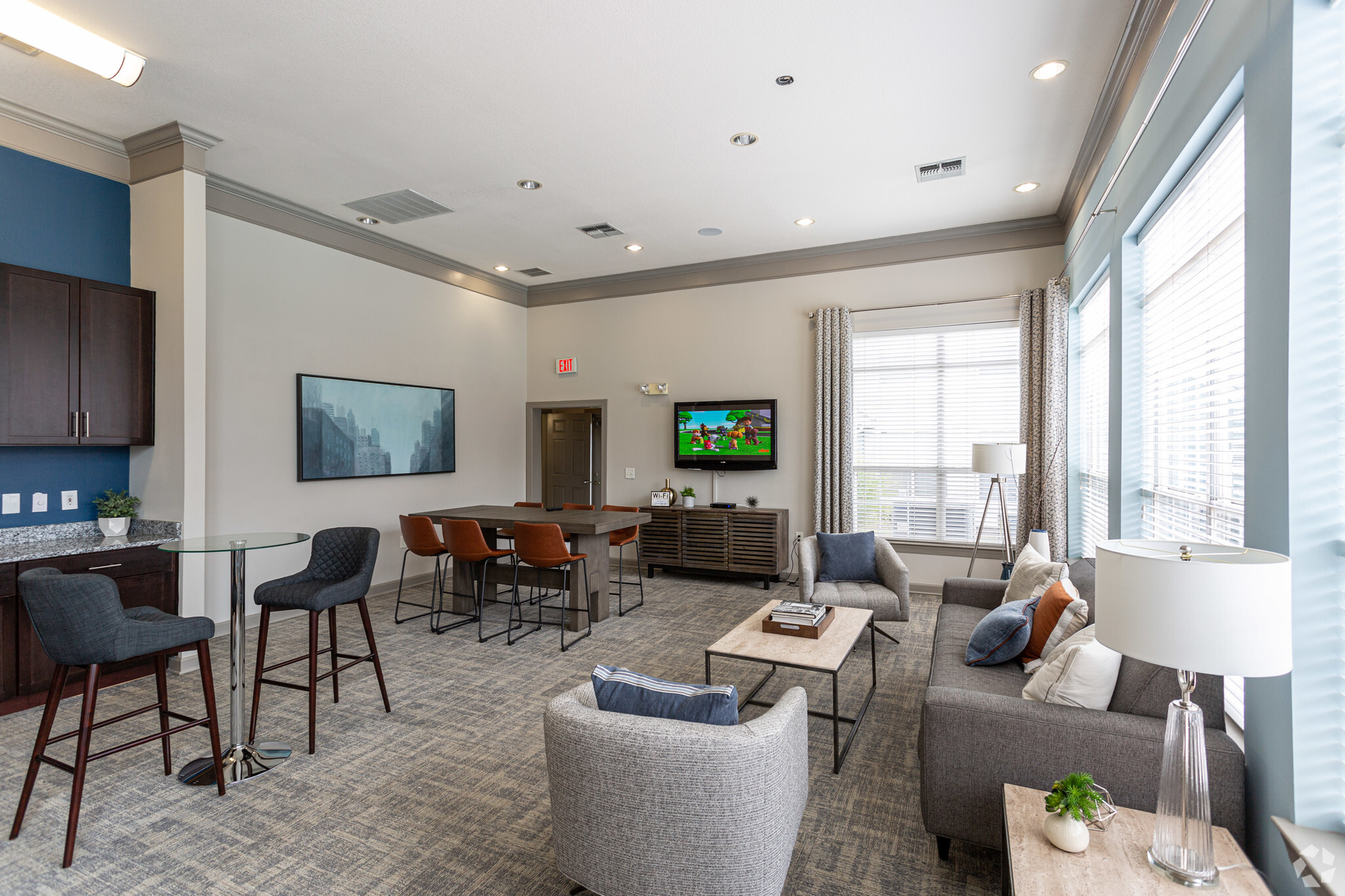 A modern community lounge featuring a seating area, bar stools, and a dining table. Windows offer natural light at Scout Landing.
