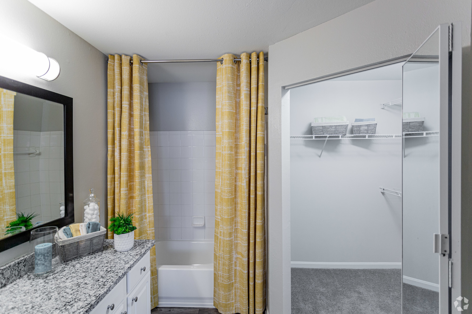 Bathroom with a granite countertop vanity, tub with gold curtains, and a walk-in closet visible through a sliding glass door at Scout Landing.