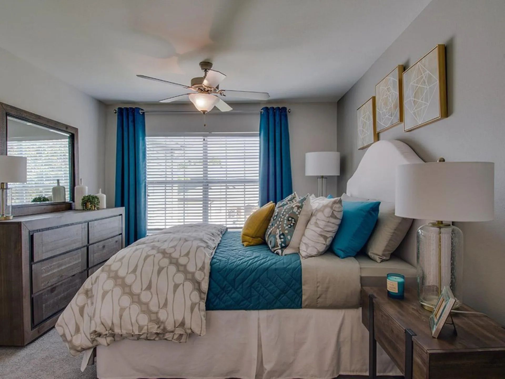 Cozy bedroom with a bed, dresser, and nightstand. Features blue curtains, white bedding, and gray walls, with decorative pillows at Scout Landing.
