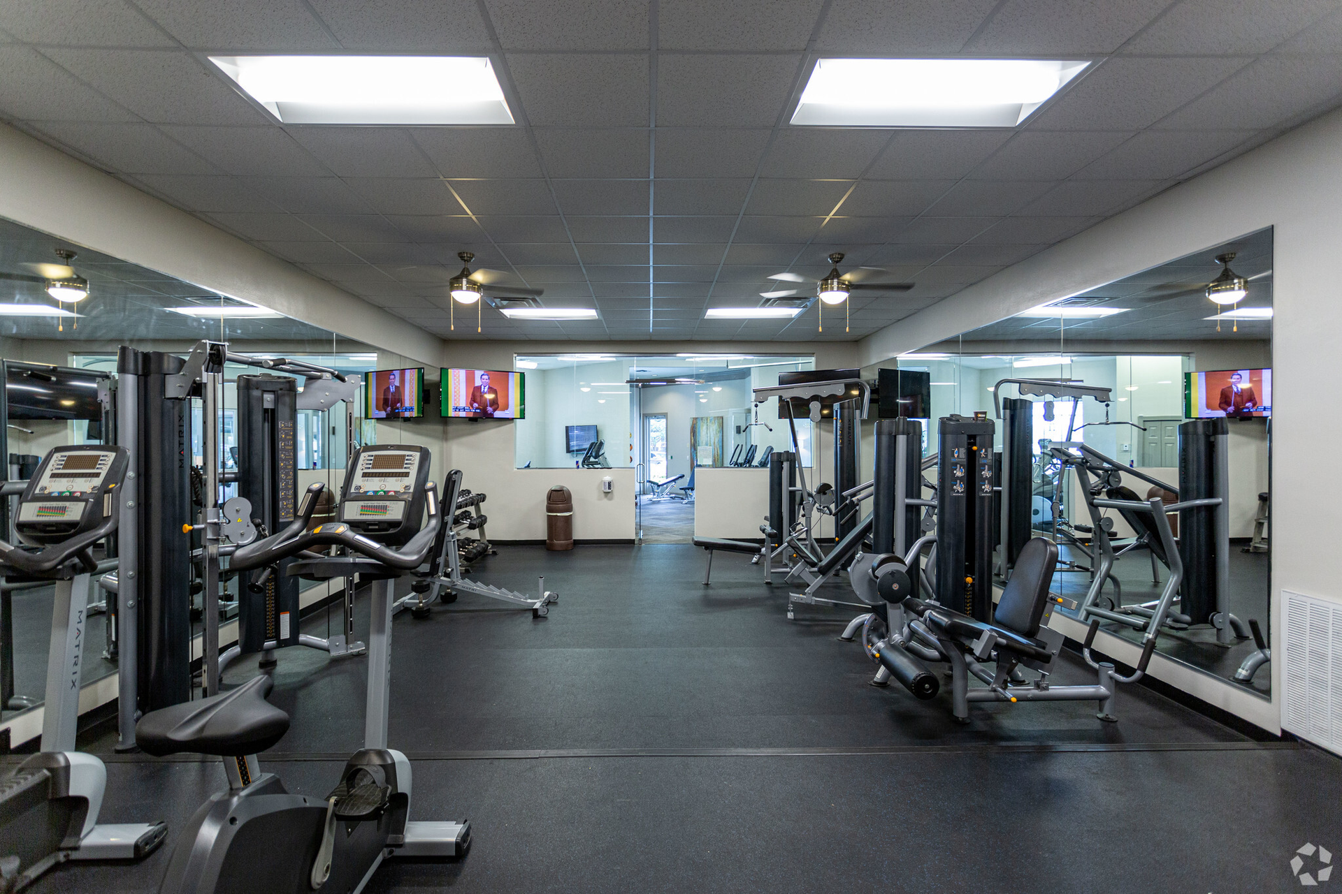 Gym interior with exercise machines, ceiling lights, mirrors, and TVs. Black rubber floor at Scout Landing.