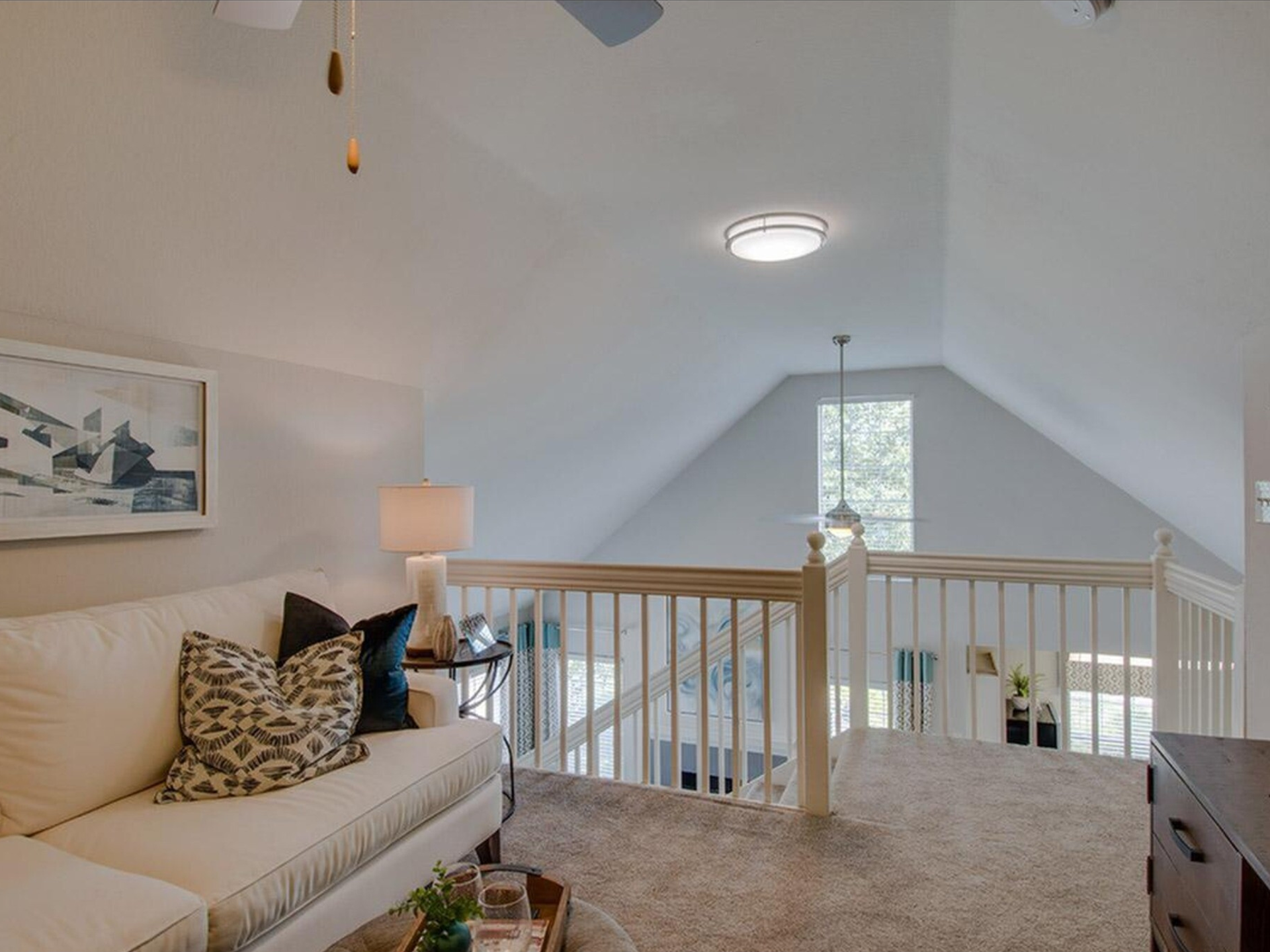 A bright loft space with a couch, railing, and window in a high-ceilinged room with neutral tones at Scout Landing.
