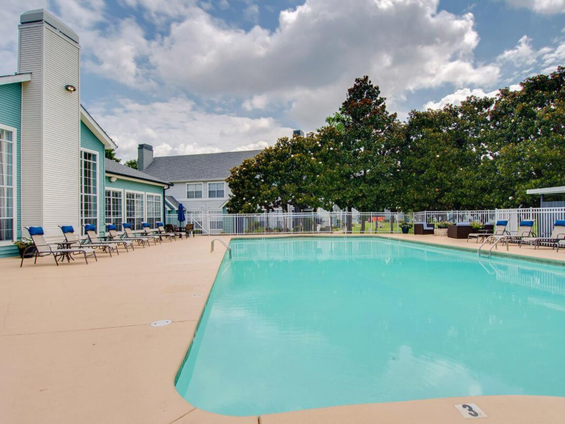 A large swimming pool is surrounded by chairs and a building.