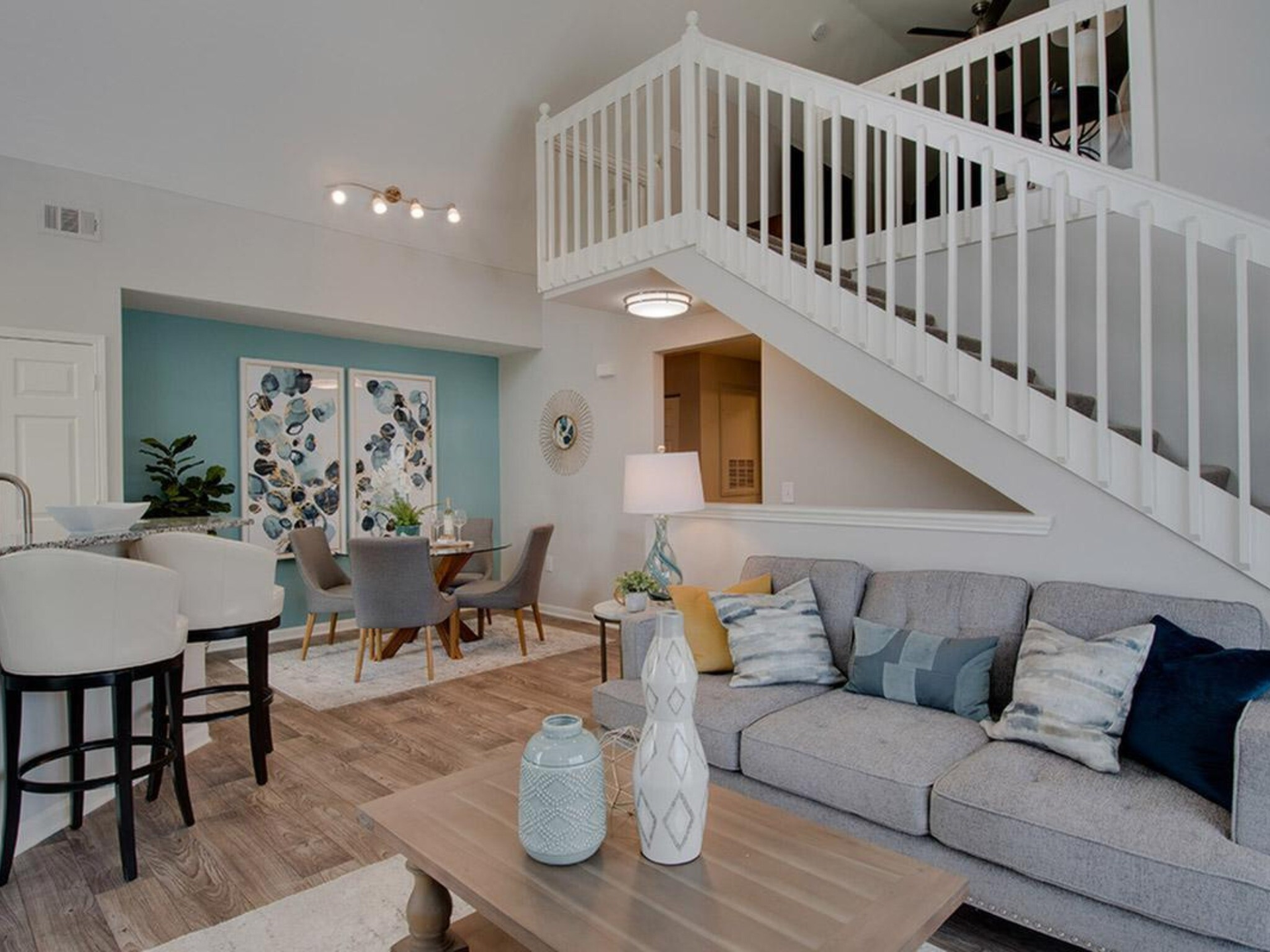 A living room with a light gray sofa, dining area, and staircase. A light blue wall with art is featured behind the dining table at Scout Landing.