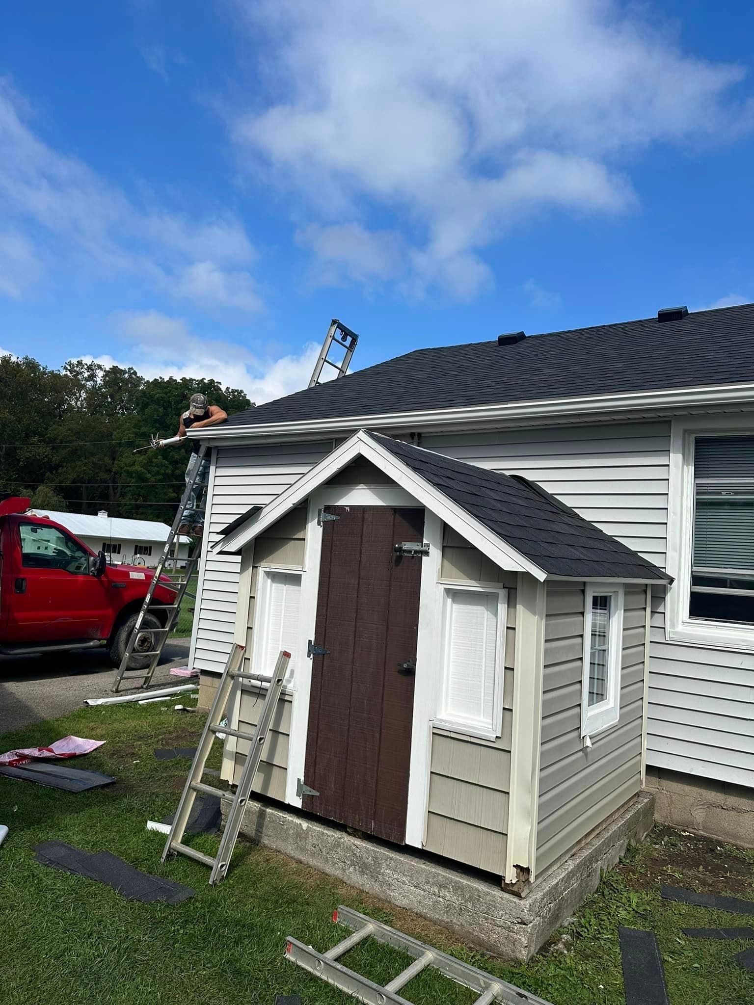 A Man Is Standing On A Ladder On The Roof Of A House - Sandusky, OH - Petrick Roofing and Remodel LLC