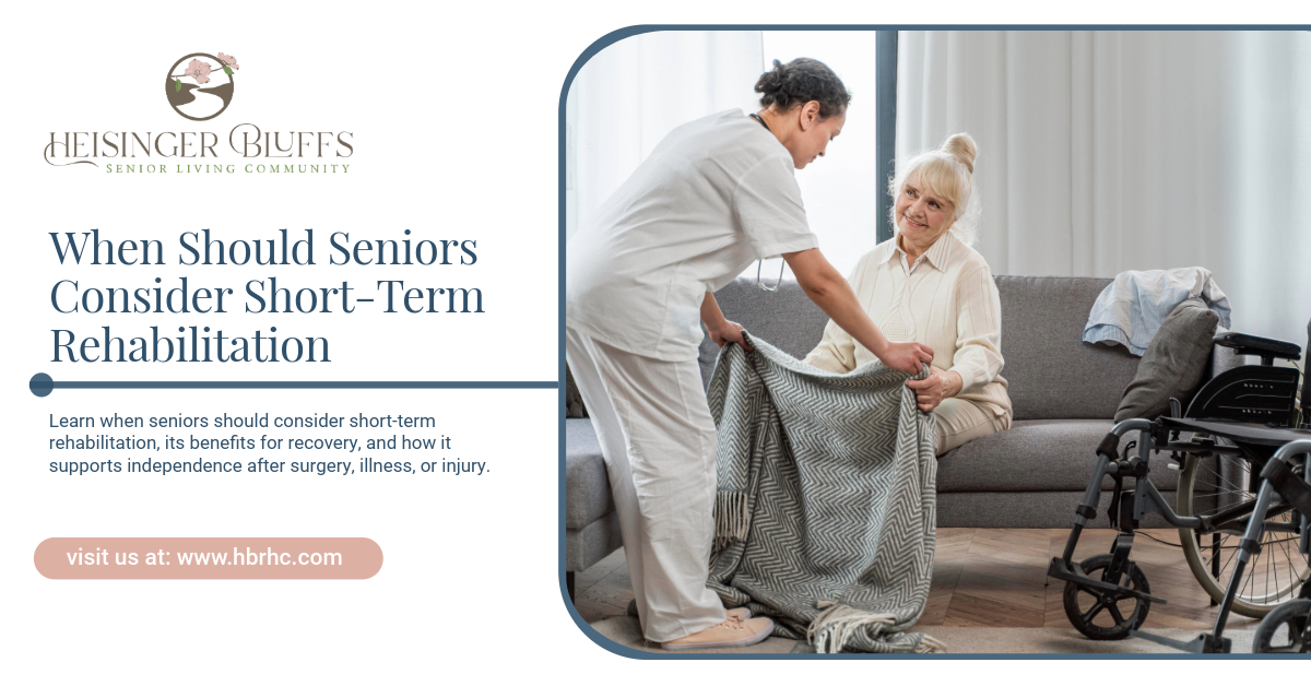 A caregiver helps an elderly person sit up, next to a sofa and wheelchair, in a living room.