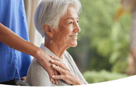 An elderly woman in a wheelchair being helped by a nurse 