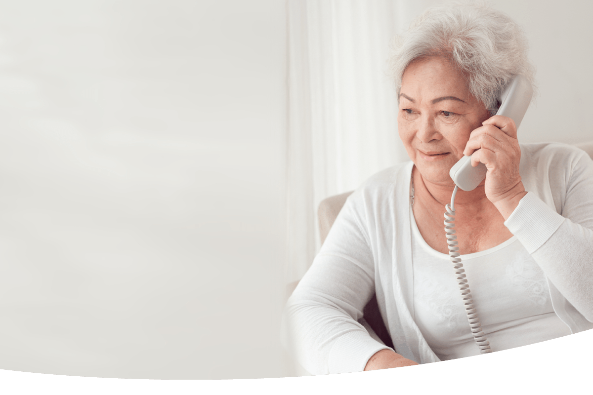 An elderly woman sitting in a chair talking to someone on a telephone 