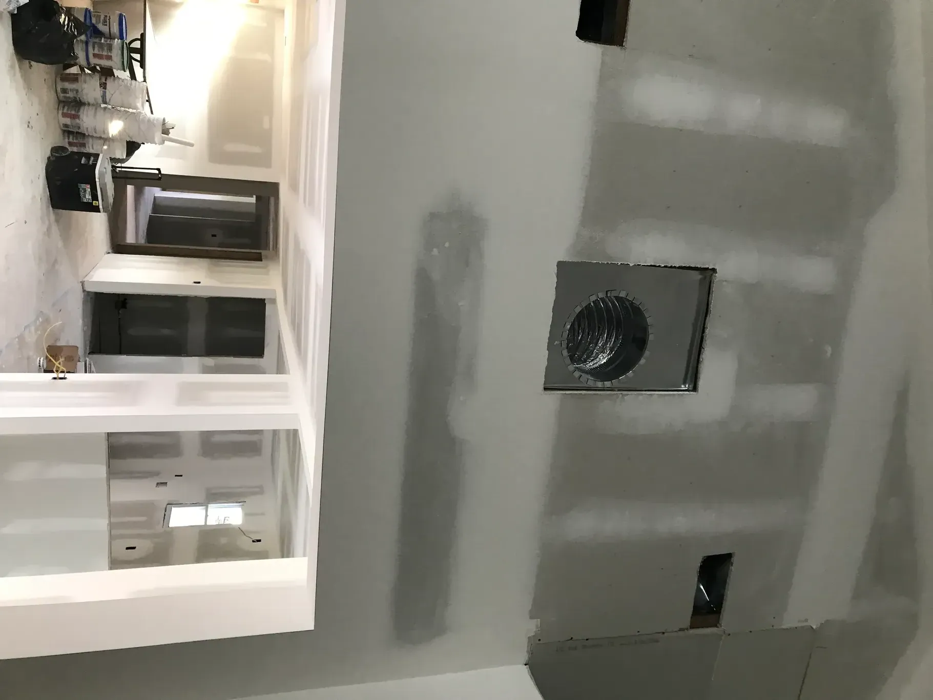 Wall with a square vent and a lower electrical outlet. Kitchen cabinetry is visible in the background.