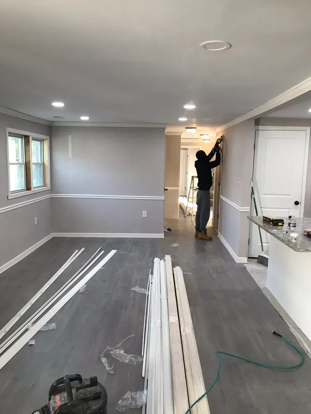 Man installing molding in a room with gray walls, flooring, and trim.