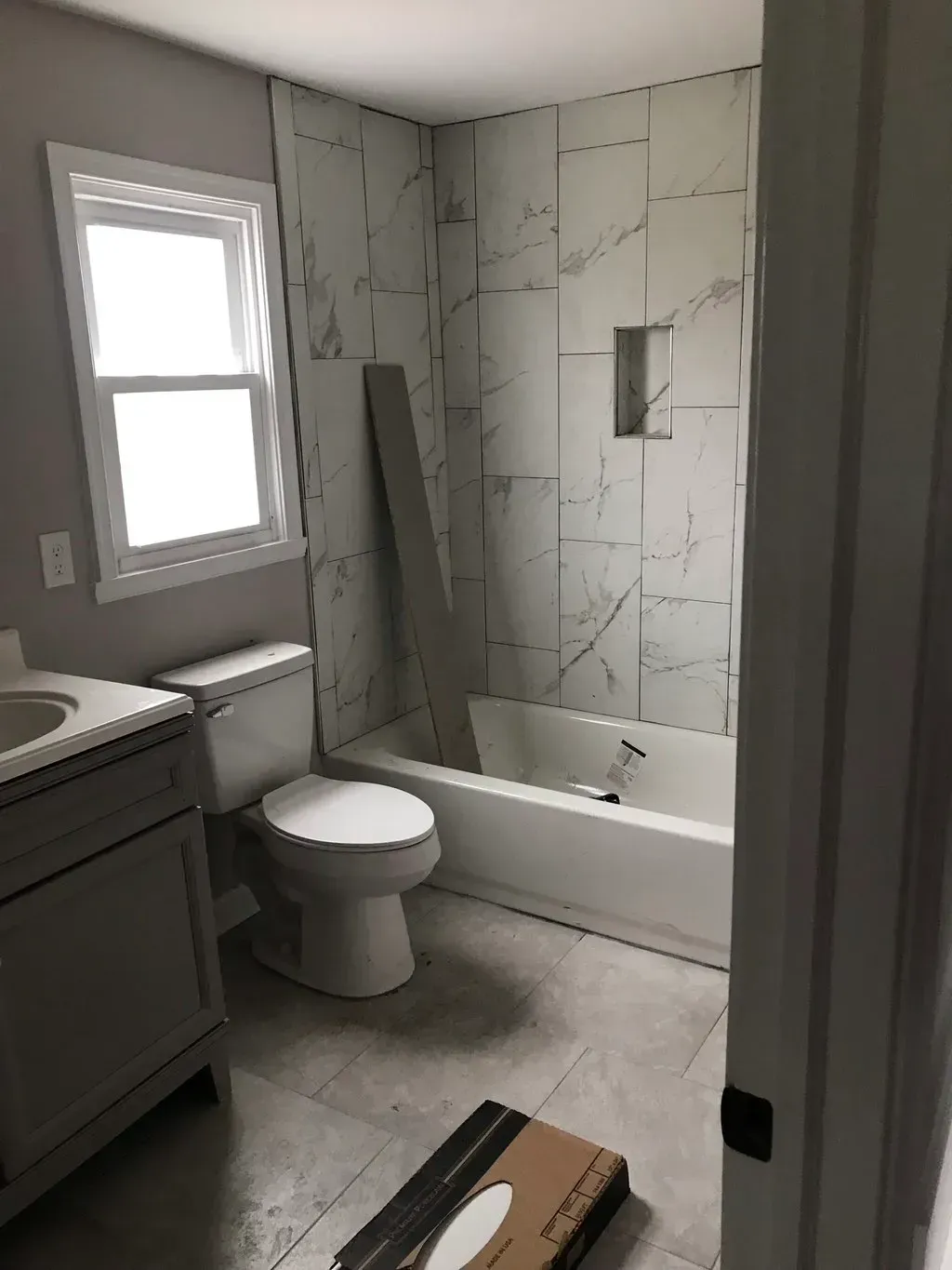Bathroom with gray vanity, white toilet, and marble-look shower tile.