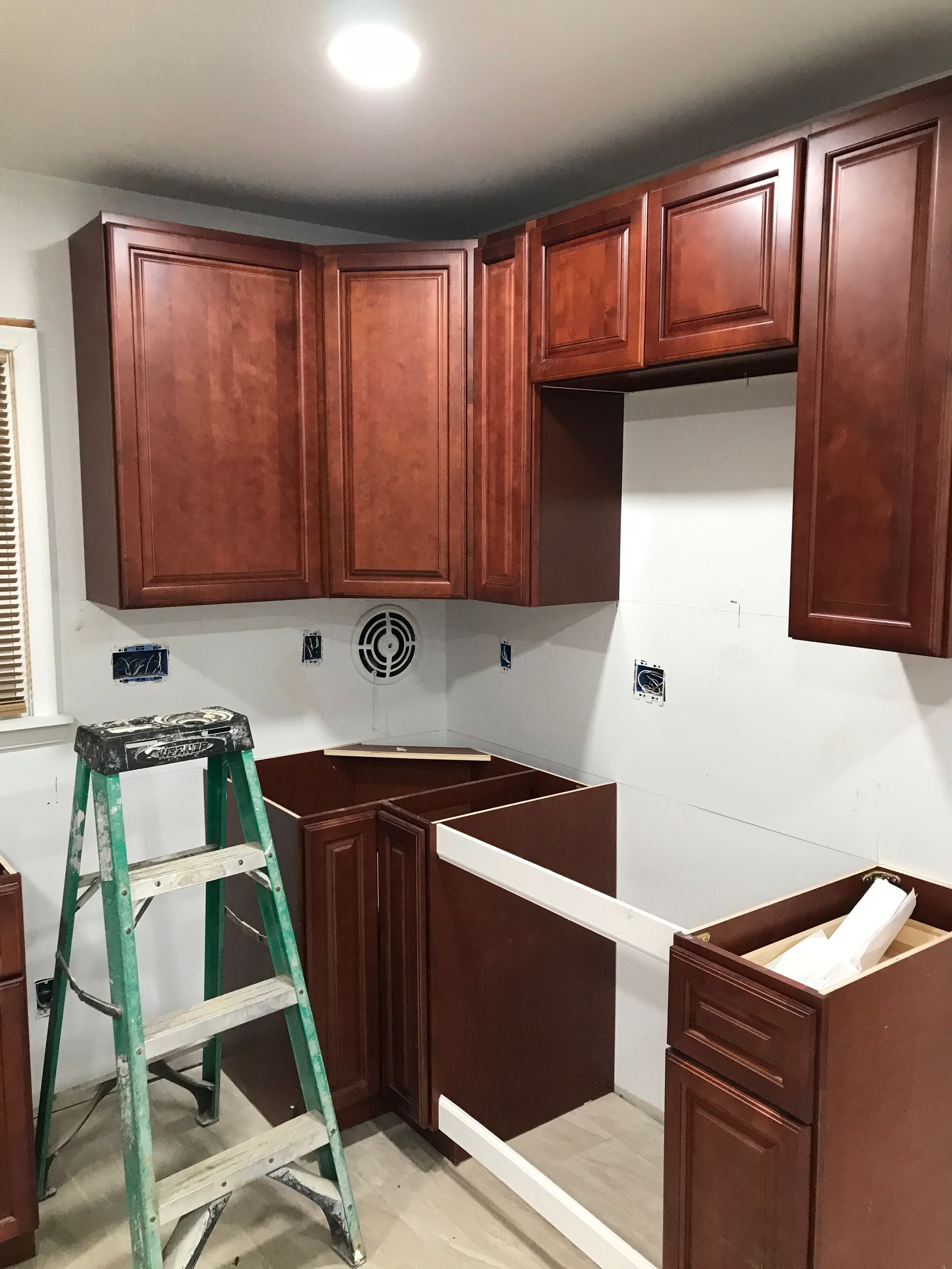 Kitchen under construction with installed brown cabinets and ladder.