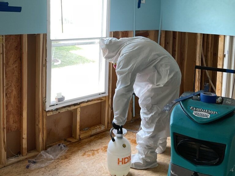 Person in protective suit sprays a wall near a window during a remediation project.
