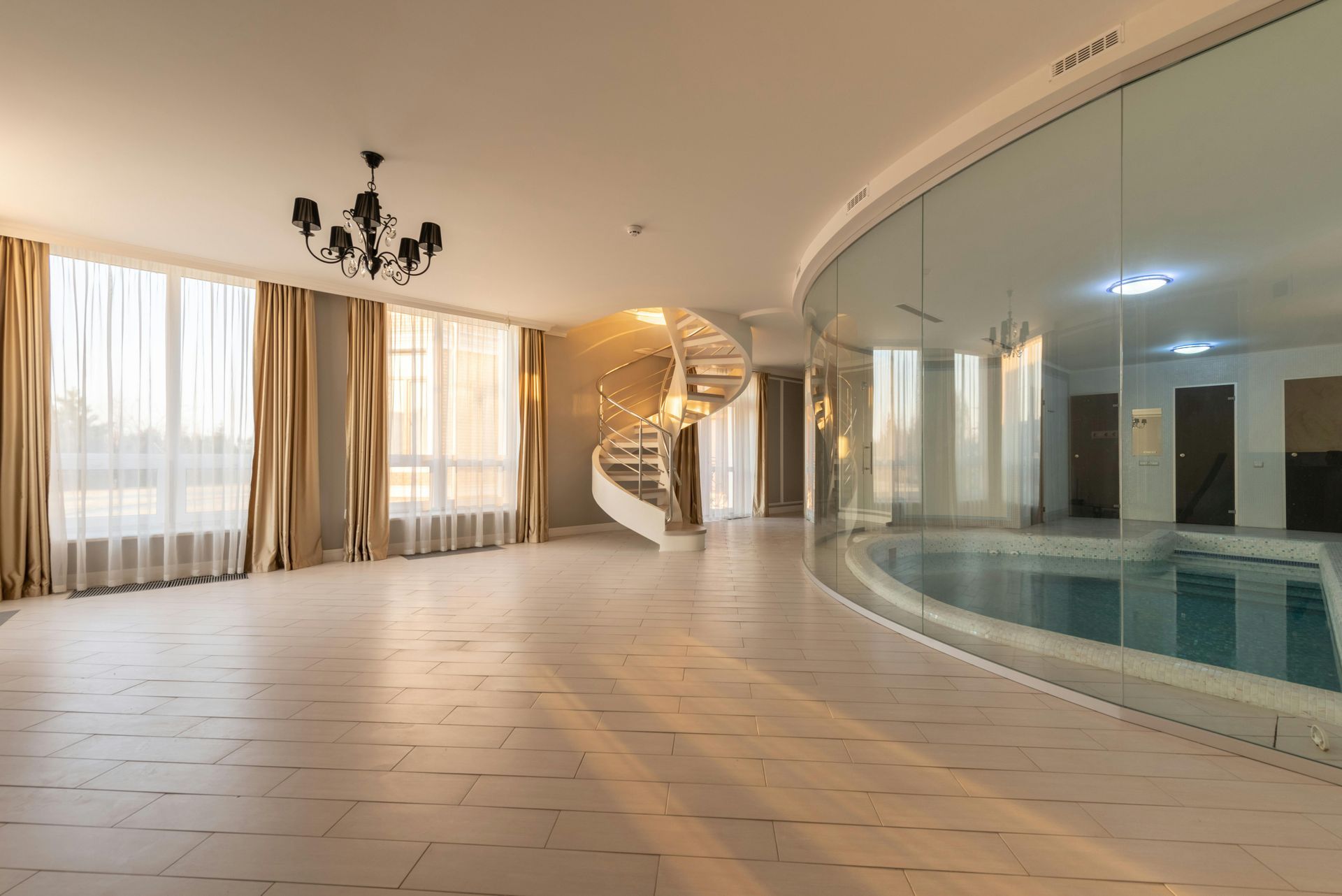 Spacious room with a spiral staircase, a pool behind glass, and large windows with golden curtains.