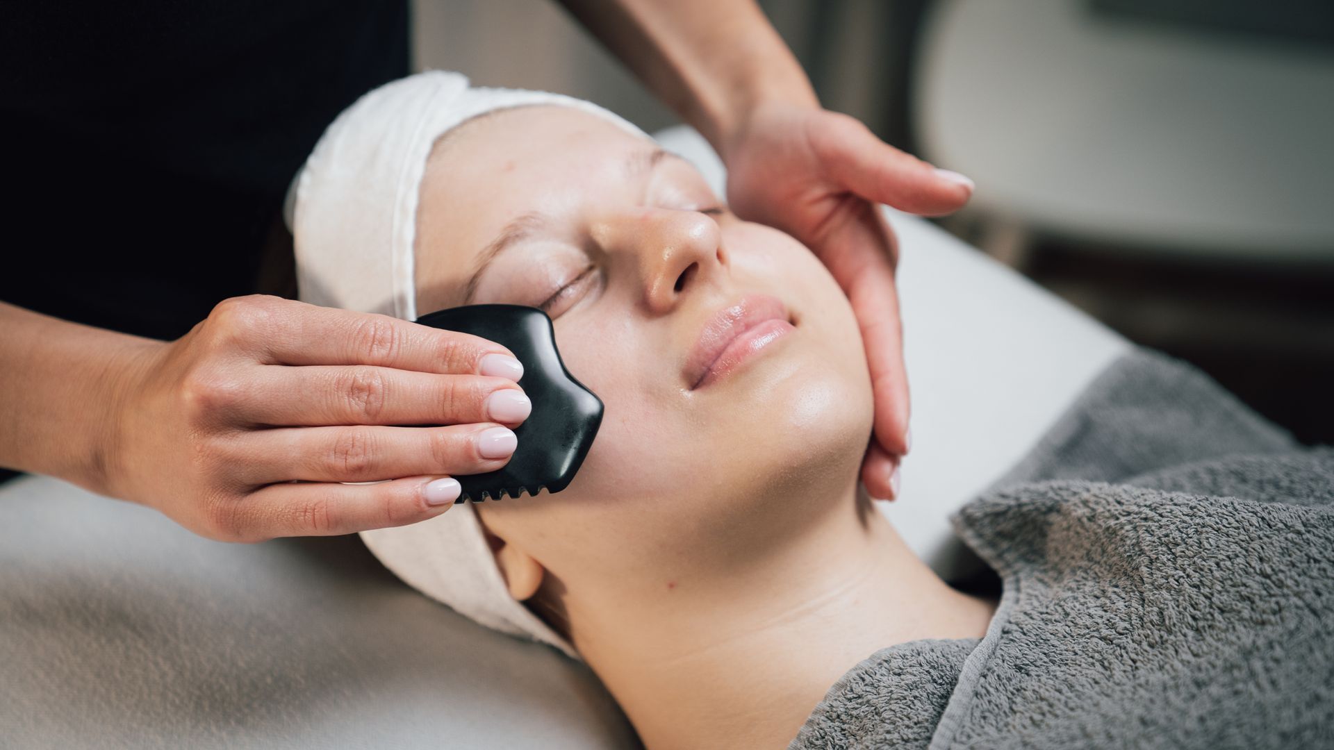 Gesichtsmassage mit einem schwarzen Stein auf der Wange einer Frau in einem Spa-Ambiente