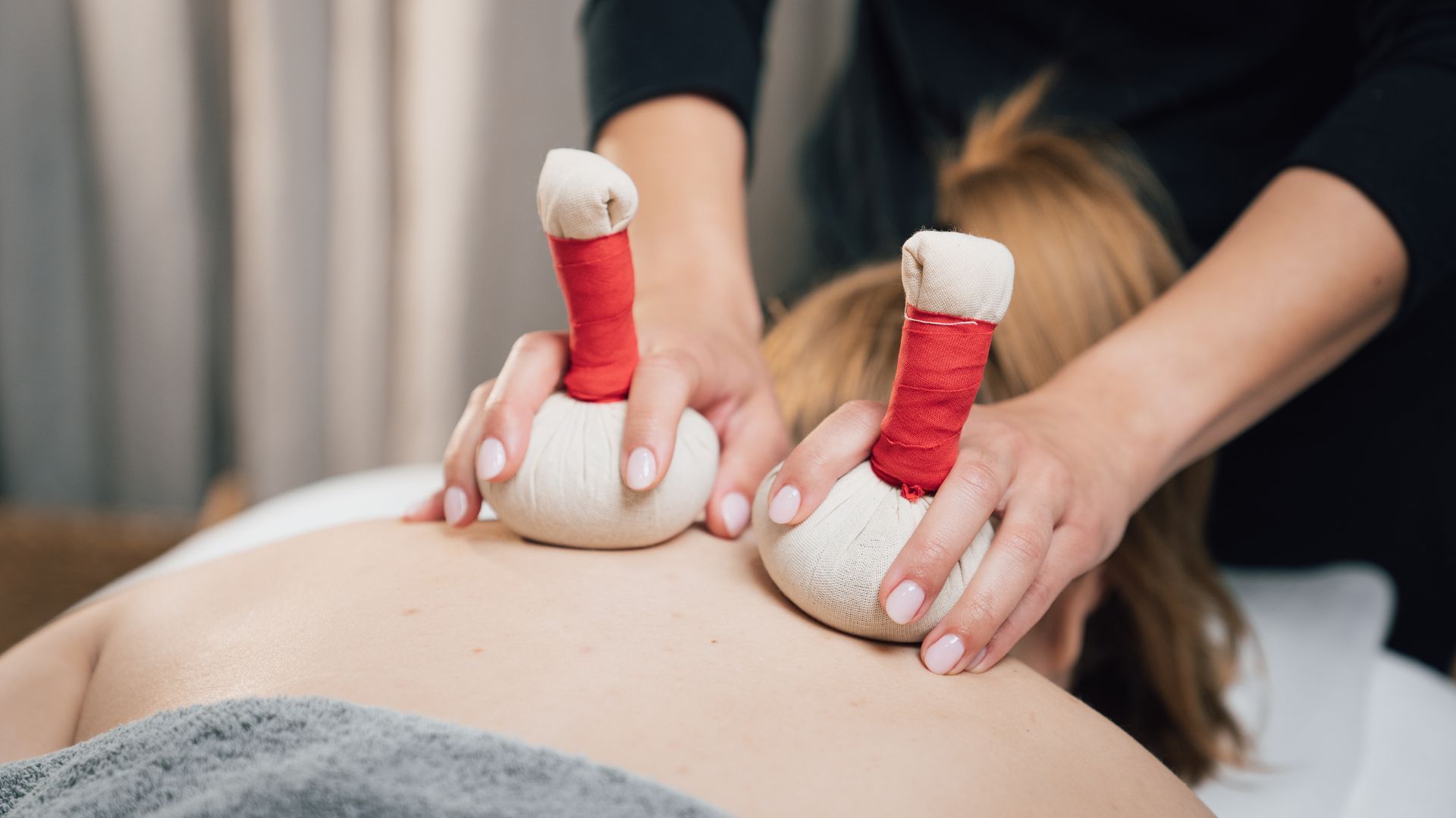 Hände, die während einer Spa-Massage mit erhitzten Steinen über einen nackten Rücken streichen.