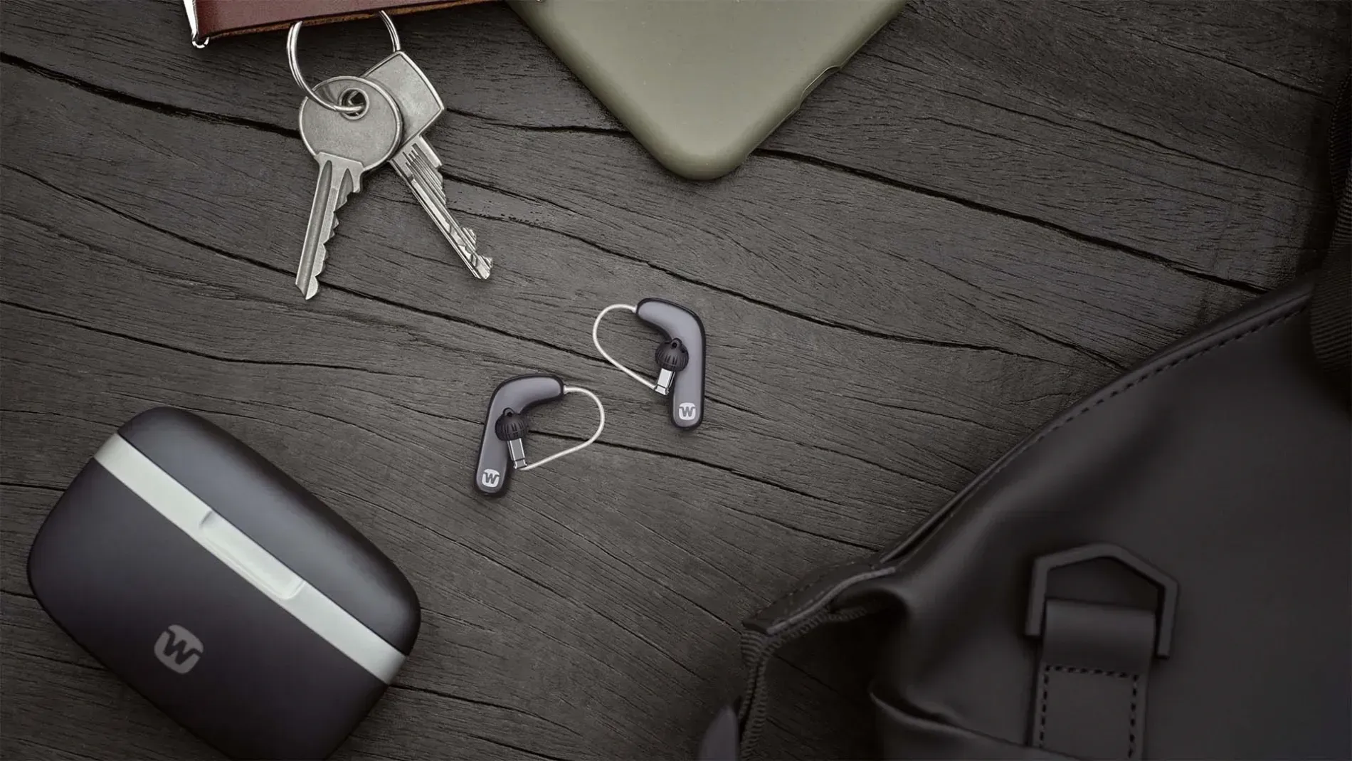 A pair of hearing aids are sitting on a table next to a bag and keys.