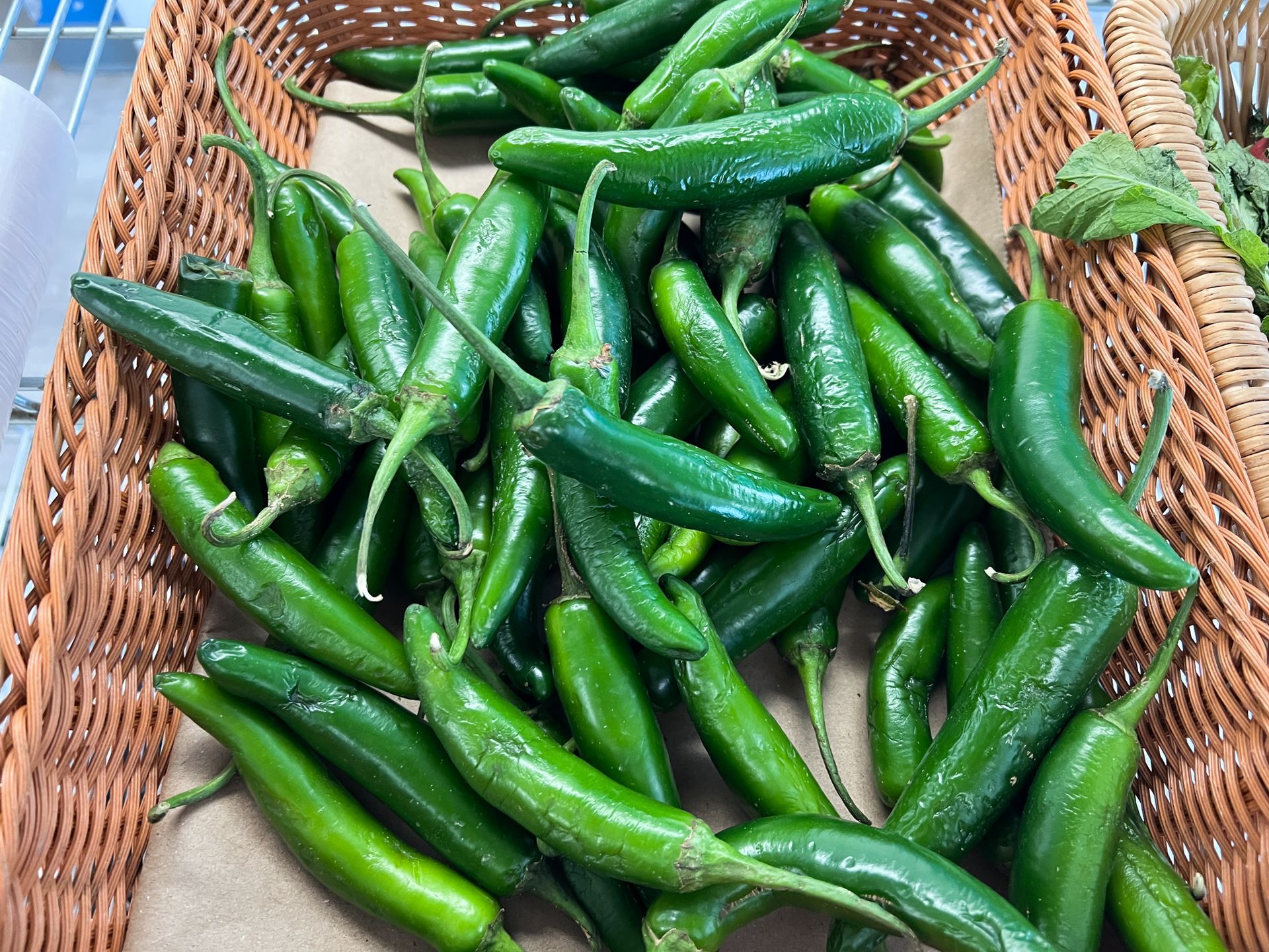 A basket filled with green peppers is sitting on a table.