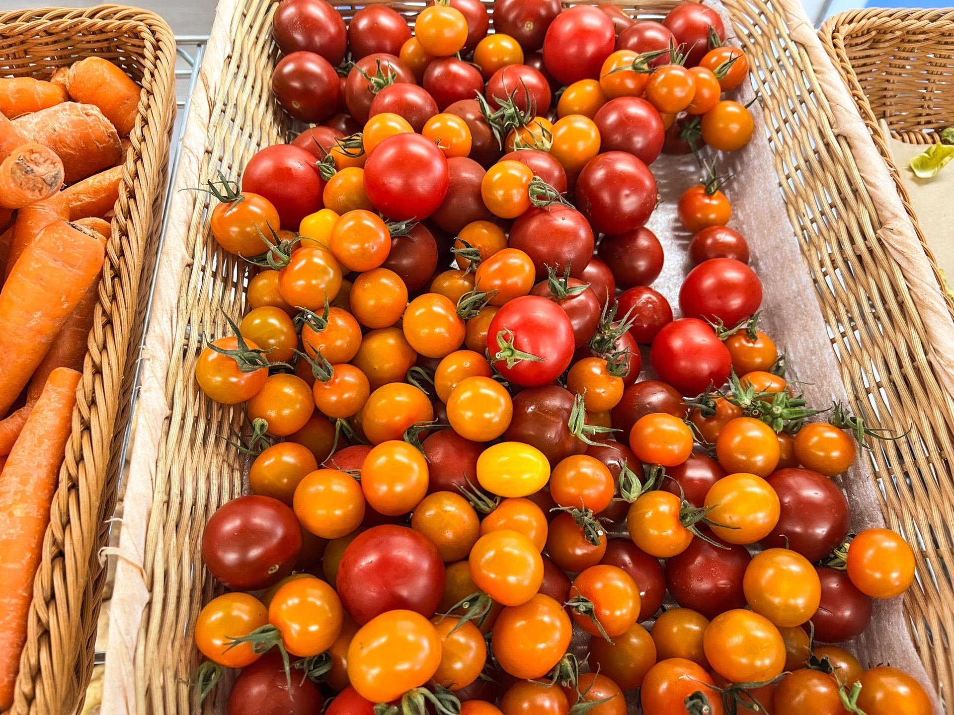 A bunch of tomatoes and carrots in wicker baskets