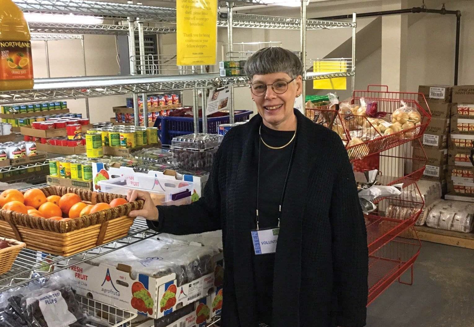 A woman is standing in a grocery store holding a basket of oranges.
