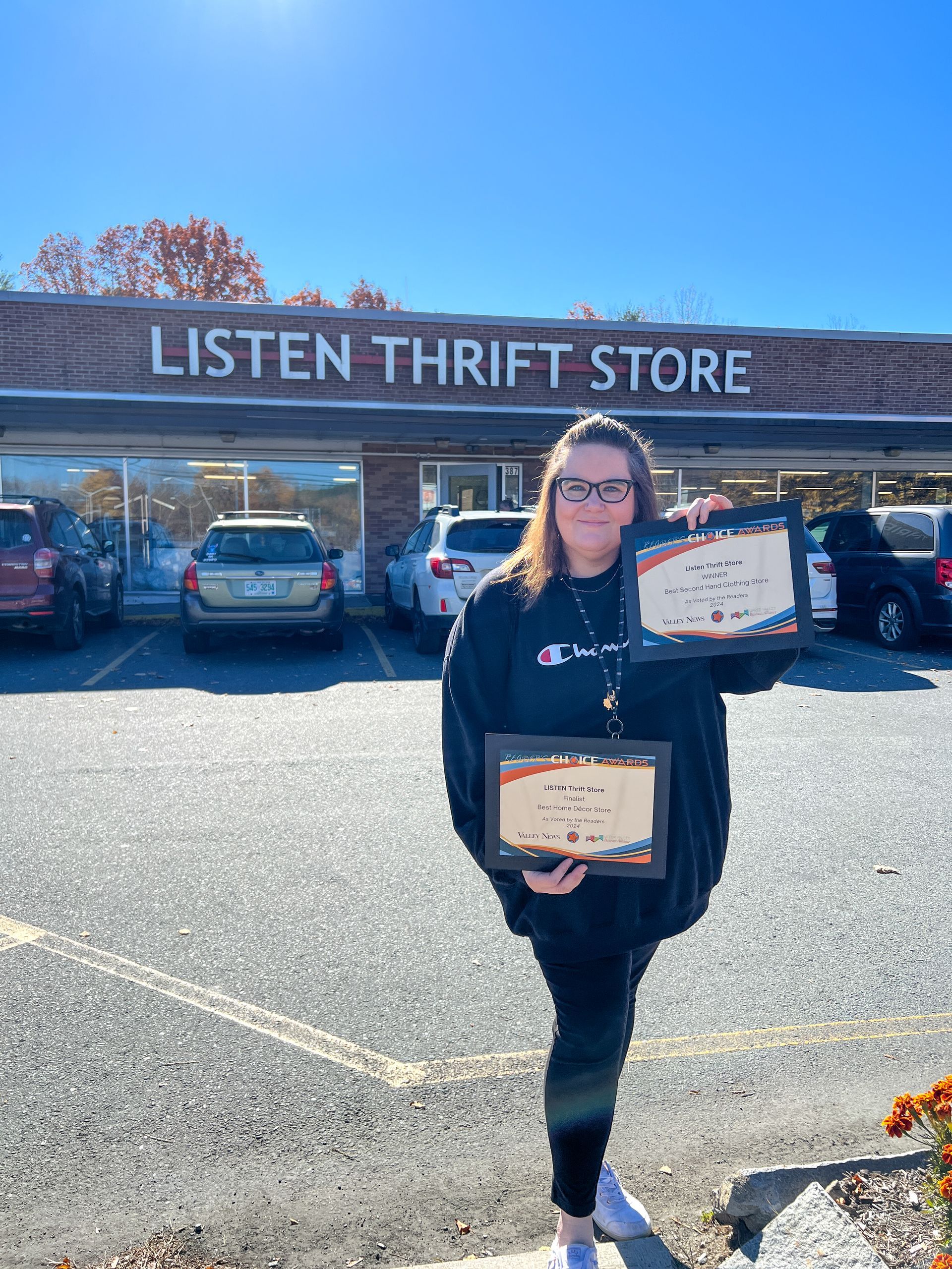 A woman is holding two certificates in front of a thrift store.