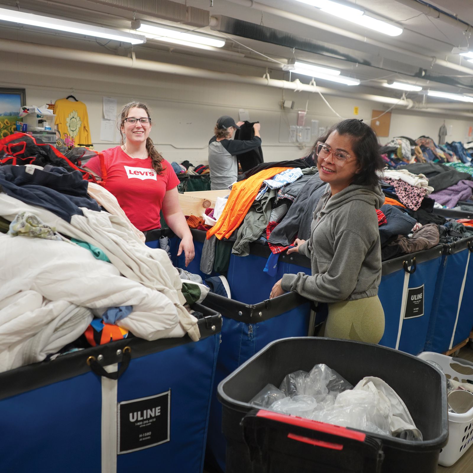 A woman wearing a red shirt that says levis is standing in front of a pile of clothes