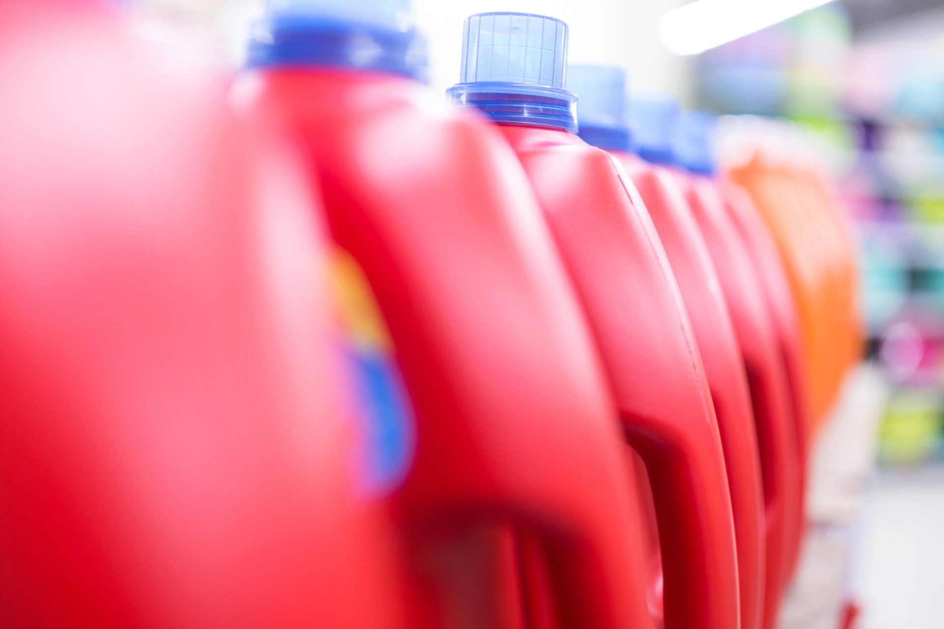 A row of red bottles of laundry detergent are lined up on a shelf in a store.