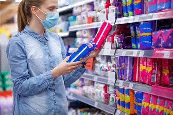 A woman wearing a face mask is buying sanitary pads in a supermarket.