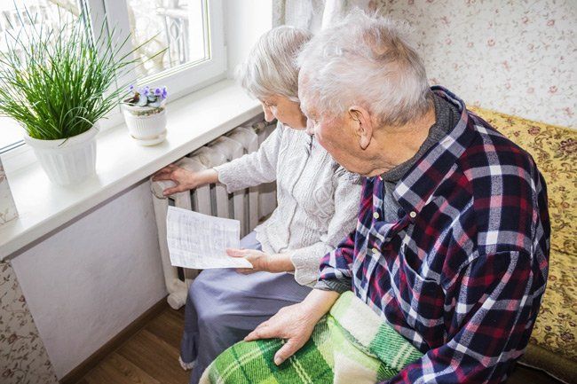 An elderly couple is sitting on a couch looking at a piece of paper.