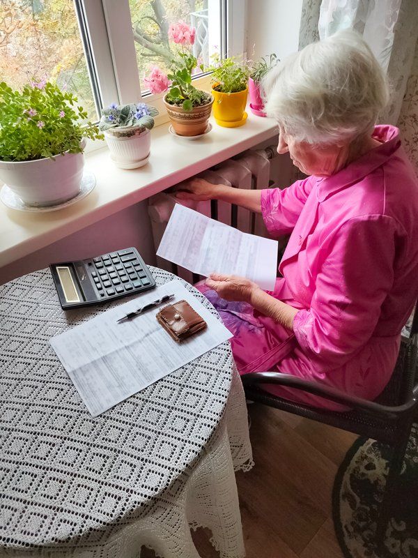An elderly woman is sitting at a table with a calculator and papers.