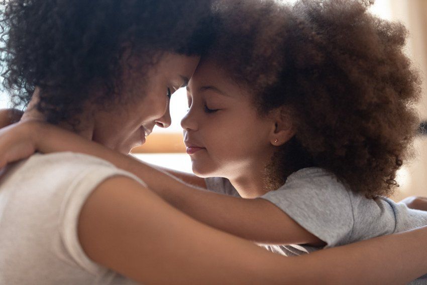 A woman and a little girl are hugging each other.
