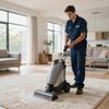 Man using carpet cleaner on a rug in a living room, water visible, sunny day.
